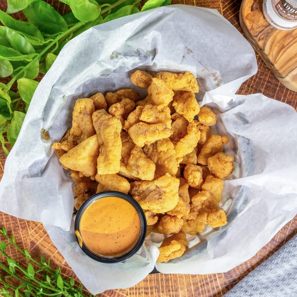 A basket of golden-fried seafood bites with a side of dipping sauce on a wooden table.