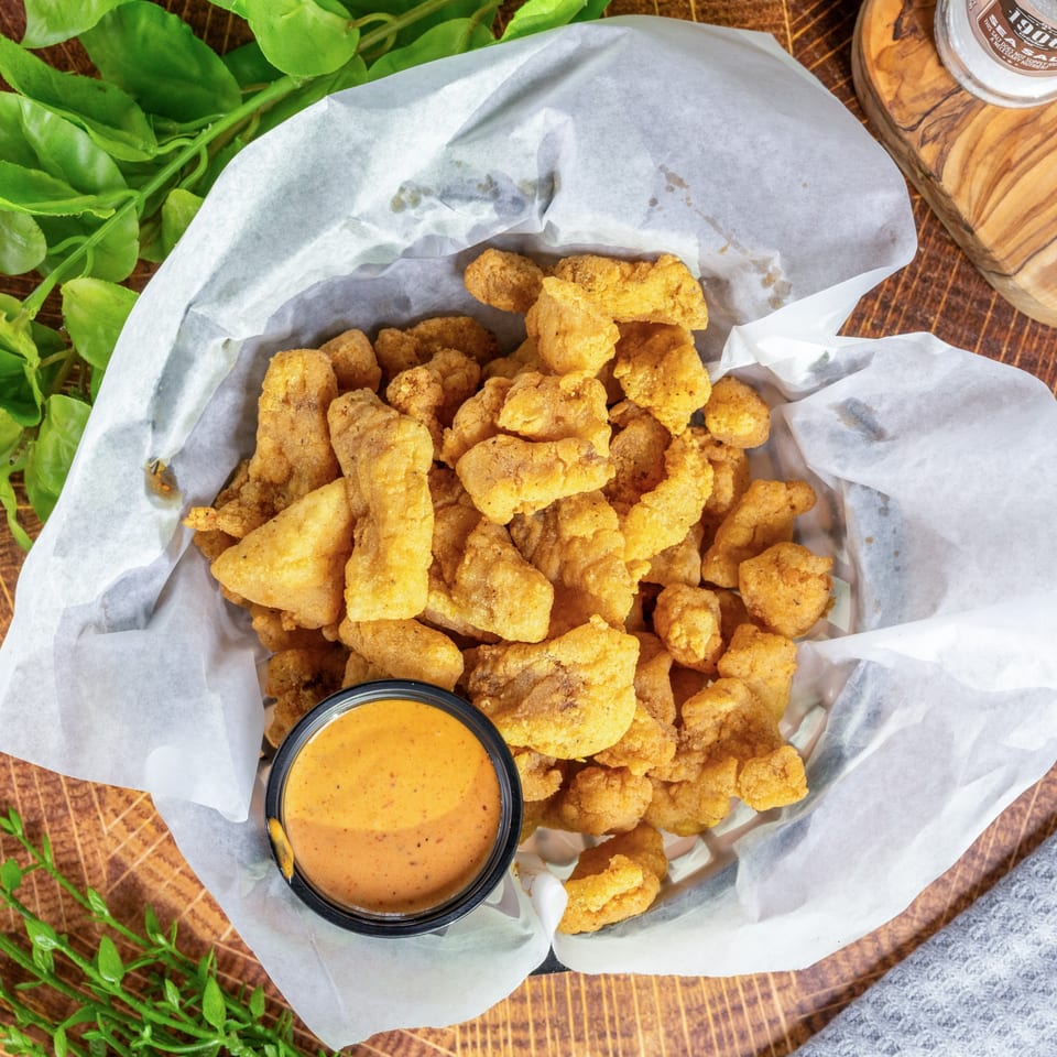 A basket of golden-fried seafood bites with a side of dipping sauce on a wooden table.