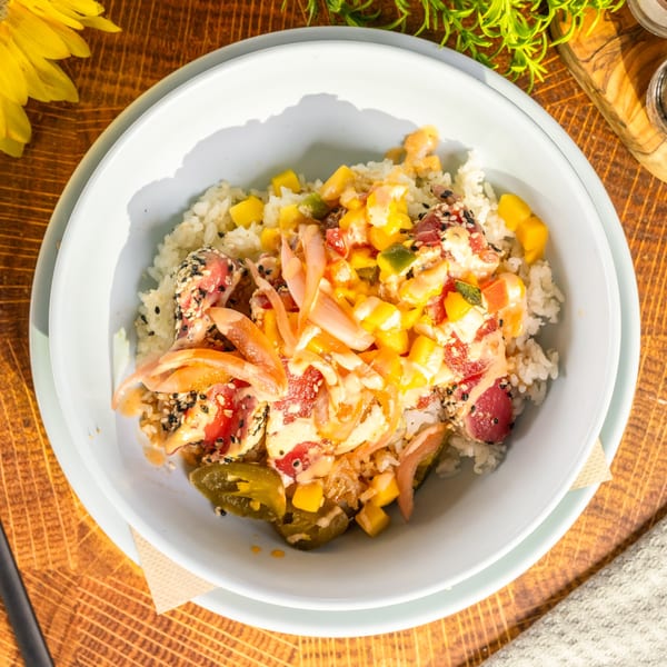 Overhead view of a seafood poke bowl with tuna, rice, mango, and pickled onions.