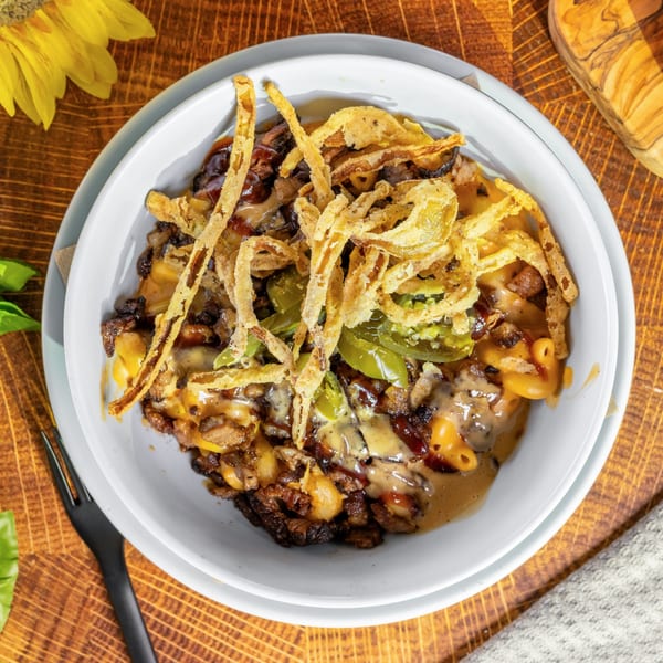 OSO's mac and cheese with steak, jalapeños, and crispy fried onions in a white bowl.