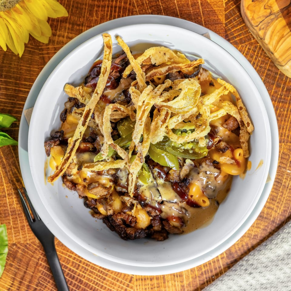 OSO's mac and cheese with steak, jalapeños, and crispy fried onions in a white bowl.