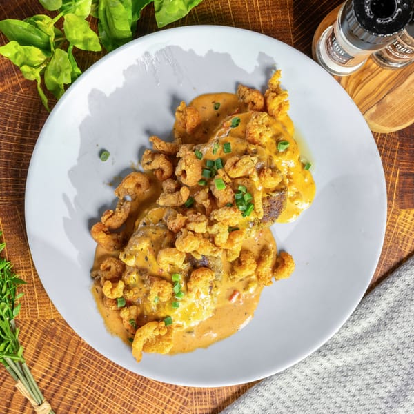 OSO's fried shrimp and grits, topped with creamy sauce and green onions, on a white plate.