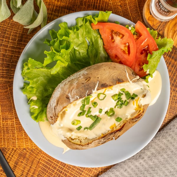 Baked potato topped with cheese sauce and chives, served with lettuce and tomato slices.