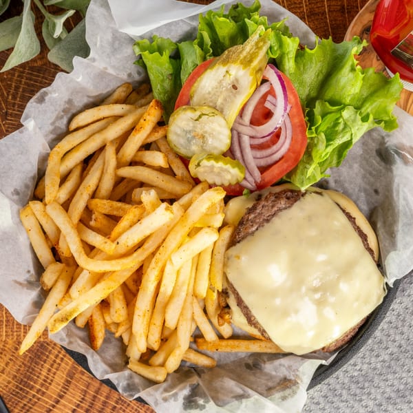 Cheeseburger with lettuce, tomato, onion, pickles, and a side of seasoned fries in a basket.